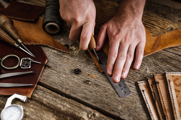 Sluiten van een schoenmaker of ambachtelijke arbeider handen. Lederen handwerktuigen op oude houten tafel. Werkplaats voor leerambacht. - Foto, afbeelding