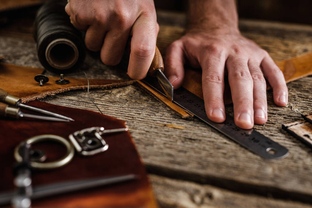 Sluiten van een schoenmaker of ambachtelijke arbeider handen. Lederen handwerktuigen op oude houten tafel. Werkplaats voor leerambacht. - Foto, afbeelding