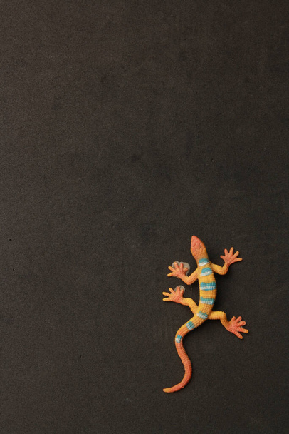 A vertical closeup shot of a lizard shaped rubber toy on a black background - 写真・画像