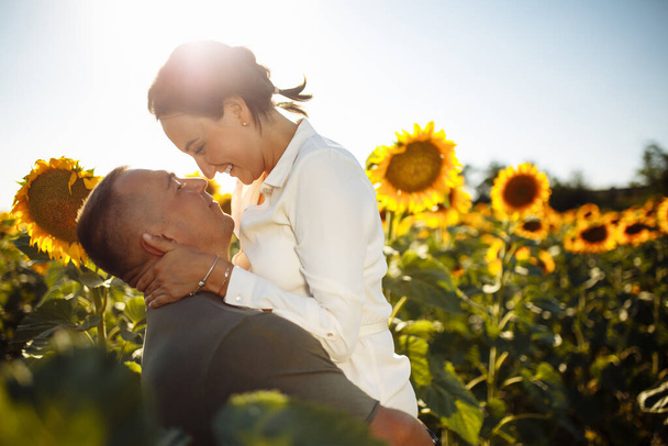 Young couple having fun during the summer day on the sunflower field. Man and woman hug and kiss and being happy showing love. Freedom, joy, unity and family values concept - Фото, зображення