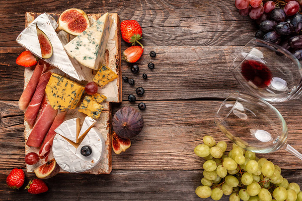 Assortment of cheeses fruits, berries and wine on a wooden table. banner, catering menu recipe place for text, top view. - Foto, immagini