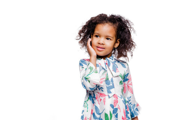 Petite jolie fille afro-américaine à la mode en robe blanche à imprimé floral détournant les yeux. Photo horizontale - Photo, image