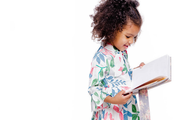 Kleine hübsche afrikanisch-amerikanische Mädchen in weißem Blumenkleid schauen auf Notizbuch - Foto, Bild