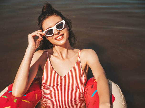 Young beautiful sexy smiling hipster woman in sunglasses.Woman in summer swimwear bathing suit swimming and lying in donut inflatable mattress.Positive female relaxing in lake water - Foto, Imagem