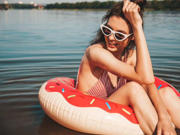 Young beautiful sexy smiling hipster woman in sunglasses.Woman in summer swimwear bathing suit swimming and lying in donut inflatable mattress.Positive female relaxing in lake water - Photo, image