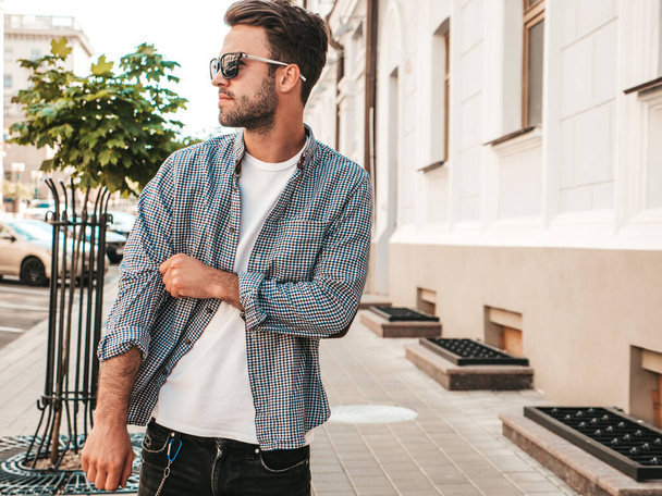 Portrait of handsome confident stylish hipster lambersexual model.Man dressed in shirt. Fashion male posing on the street background in sunglasses - Fotografie, Obrázek