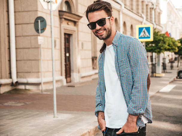 Portrait of handsome smiling stylish hipster lambersexual model.Man dressed in shirt. Fashion male posing on the street background in sunglasses - 写真・画像