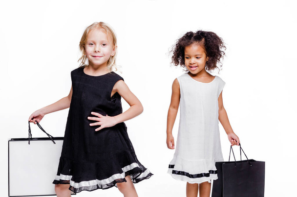 Pequenas meninas da moda namoradas de duas nacionalidades diferentes posando em um fundo branco com sacos de compras
. - Foto, Imagem