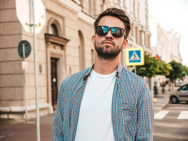 Portrait of handsome confident stylish hipster lambersexual model.Man dressed in shirt. Fashion male posing on the street background in sunglasses - Fotografie, Obrázek