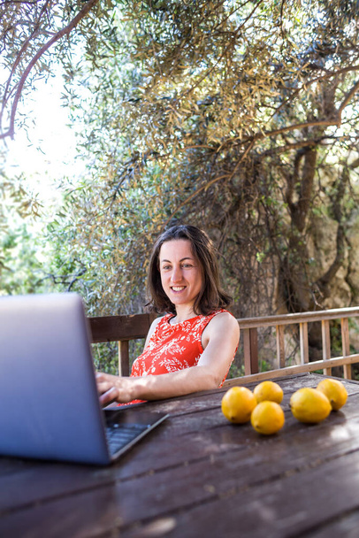 Egy vörös ruhás nő egy faház teraszán dolgozik, egy lány belenéz egy laptopba, távolsági oktatás, Freelancer a ház verandáján dolgozik, Távmunka a karantén alatt. - Fotó, kép