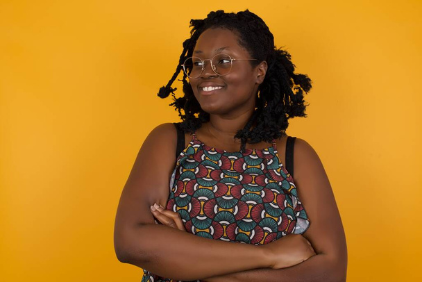 Portrait of dreamy rest relaxed Young beautiful afro american woman wearing glasses over yellow background  crossing arms looks good  - Photo, Image