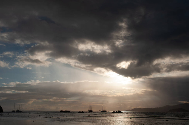 夕日の間にセーリングボートとインド洋の上に雲と太陽の光を持つ劇的な空. - 写真・画像
