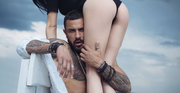 Man holding woman with sexy hot ass. Strong muscular tattooed bearded man holding his sexy fit woman with hot butt isolated at grey background. Eternal love and trust concept. - Valokuva, kuva