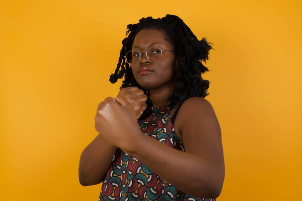 Mladá krásná afro americká žena nosí brýle přes žluté pozadí připraven k boji s gestem obrany pěsti, rozzlobený a rozčilený obličej, strach z problému. - Fotografie, Obrázek