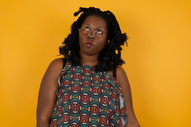 Young beautiful afro american woman wearing glasses over yellow background  making fish face with lips, crazy and comical gesture. Funny expression. - Photo, Image