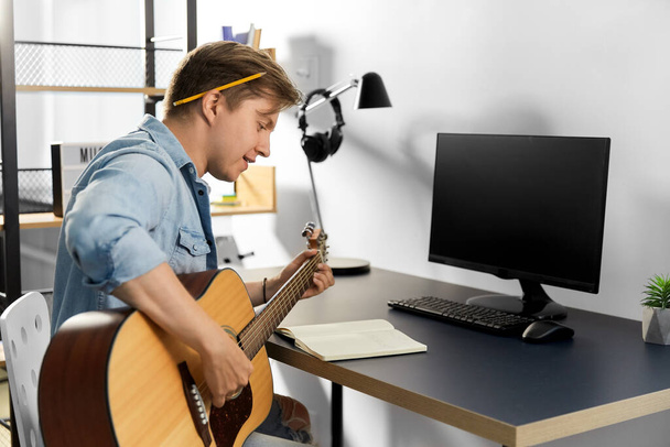 young man with music book playing guitar at home - Foto, Imagem