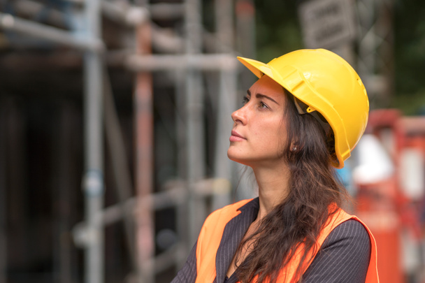 Retrato de perfil de una atractiva trabajadora de fábrica con un casco protector amarillo y mirando a un lado - Foto, imagen