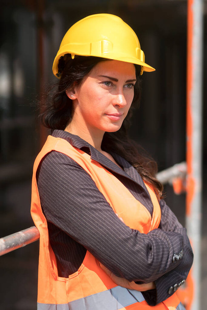 保護ヘルメットを身に着けている美しい女性工場労働者の肖像と交差腕で屋外でポーズ安全ベスト - 写真・画像