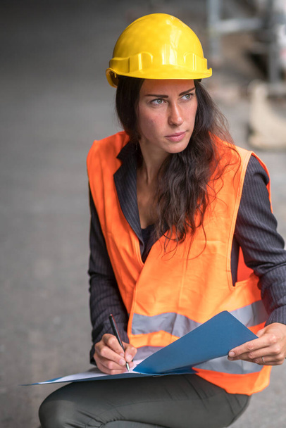 Assorbita ingegnere civile donna indossando casco di sicurezza e giubbotto controllo ufficio cianografie  - Foto, immagini