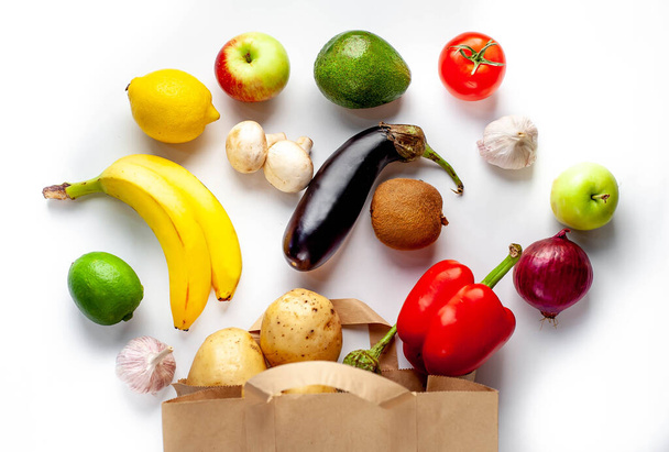 bovenaanzicht op diverse groenten en fruit met papieren zak op witte achtergrond - Foto, afbeelding