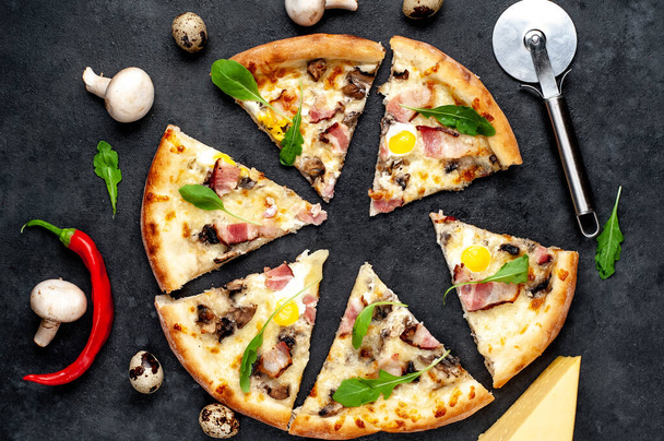 Fette divise di pizza con pancetta, olive, formaggio, uova e taglierina con ingredienti su fondo scuro - Foto, immagini