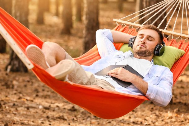 Jeune homme écoutant de la musique tout en se relaxant dans l'hamac à l'extérieur - Photo, image