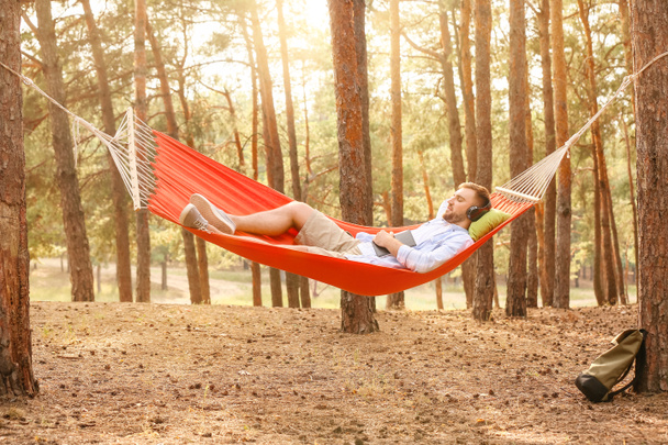 Young man listening to music while relaxing in hammock outdoors - Photo, Image