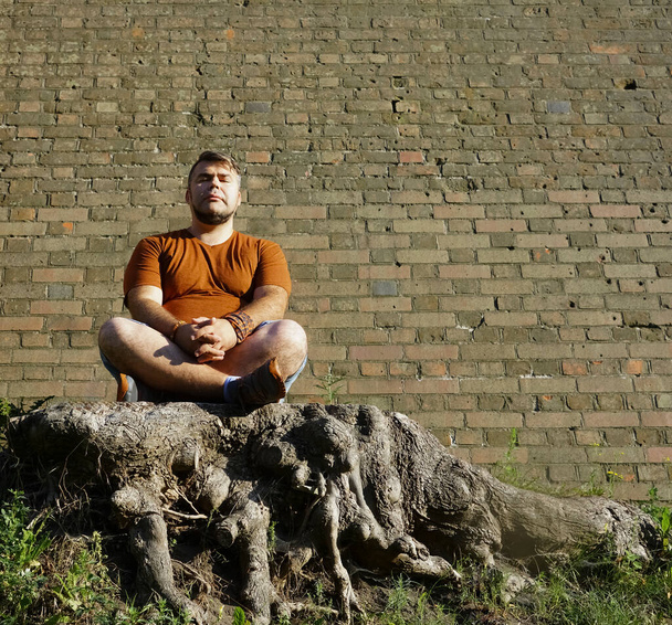 Young handsome man sitting in the woods with closed eyes, yoga pose for meditation. closed eyes - Photo, Image