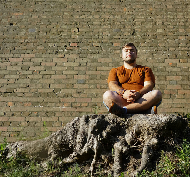 Young handsome man sitting in the woods with closed eyes, yoga pose for meditation. closed eyes - Фото, зображення