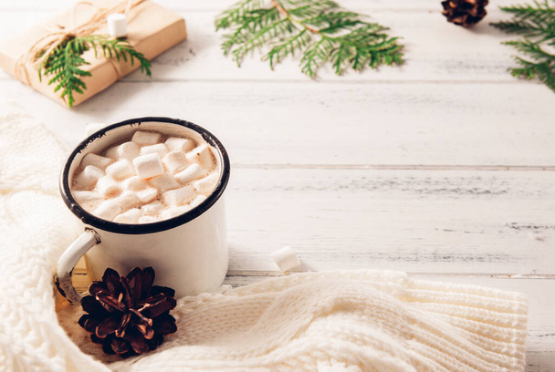 cocoa mug with marshmallows, white sweater, cones, gift box, green branches of thuja, fir branches on a white wooden background, hot winter drink - Φωτογραφία, εικόνα