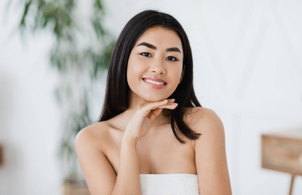 Junge asiatische Frau mit perfekter Haut, die ihr Kinn berührt - Foto, Bild