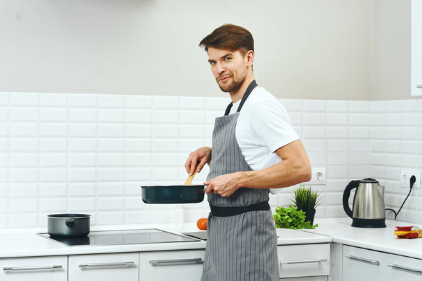 Um chef masculino de aventais cinzentos está segurando uma frigideira em suas mãos cozinhando comida
  - Foto, Imagem