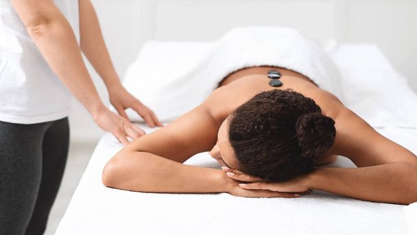 Mujer afroamericana descansando durante el masaje de piedra caliente en el spa - Foto, Imagen