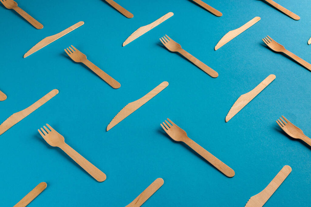 Patrón de tenedores y cuchillos desechables ecológicos de madera sobre fondo azul - Foto, Imagen