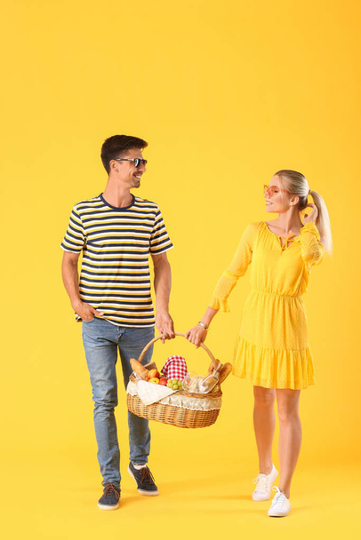 Молодая пара с пищей для пикника в корзине на цветном фоне - Фото, изображение