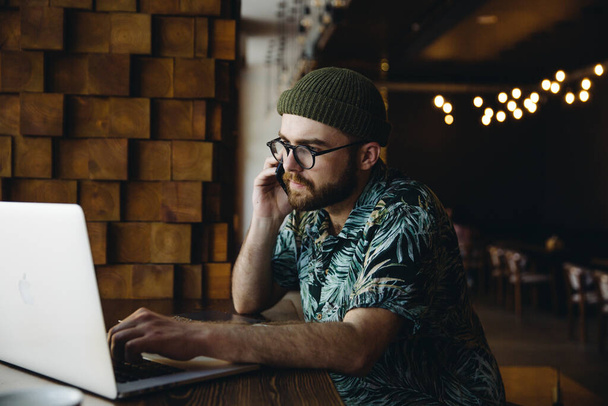 Портрет молодого красивого розумного успішного бородатого чоловіка-хіпстера, який телефонує по телефону в кафе
 - Фото, зображення