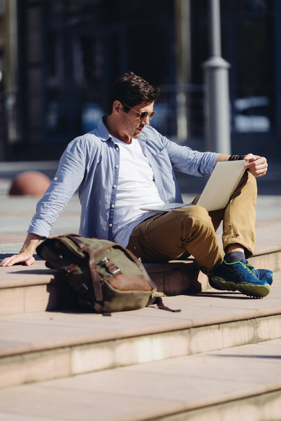 Вертикальний відвертий знімок красивого стильного чоловіка, що сидить у місті і дивиться на ноутбук
 - Фото, зображення