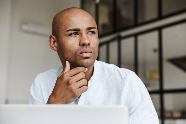 Photo closeup of serious african american man working with laptop and thinking in living room - Photo, Image