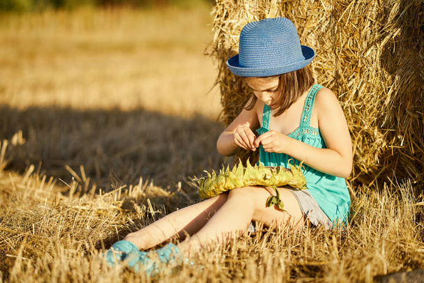adorable girl eating sunflower seeds on mown rye in the field - Fotó, kép