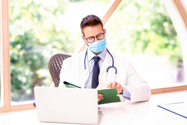 Portrait of male doctor wearing face mask and working on laptop. - Фото, изображение