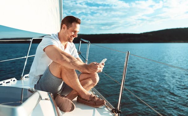 Mies käyttää älypuhelinta istuu kannella Purjehdus merellä Ulkona - Valokuva, kuva