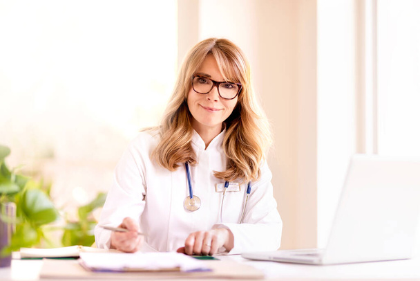 Portrait shot of smiling female doctor sitting at desk  - Photo, Image