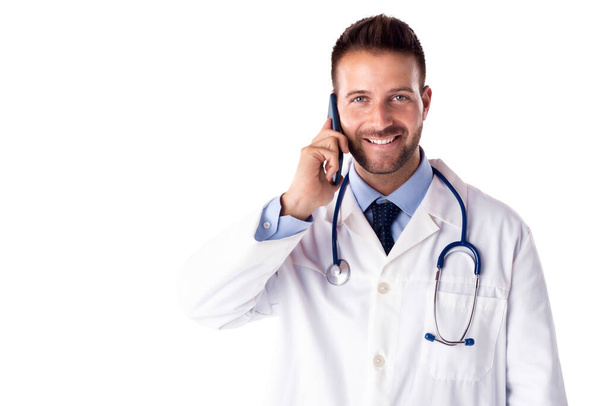 Shot of smiling male doctor talking with somebody on his mobile phone while standing at isolated white background. Copy space. - Fotografie, Obrázek