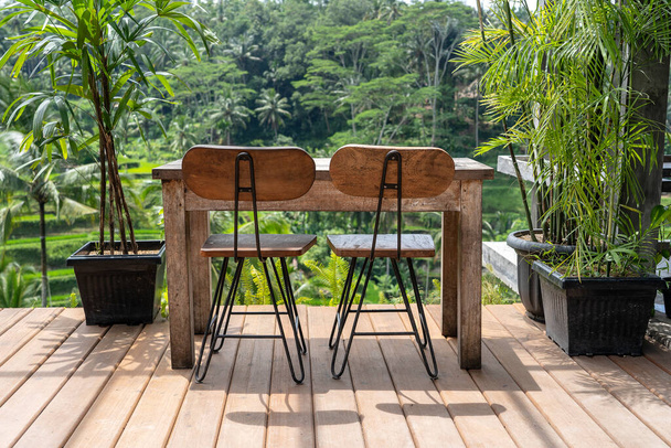 Wooden table and chairs in empty tropical cafe next to rice terraces in island Bali, Indonesia, close up - Photo, Image