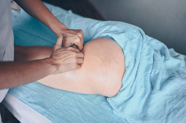 Νεαρή αγνώριστη γυναίκα ξαπλωμένη στο τραπέζι του μασάζ και απολαμβάνοντας το θεραπευτικό μασάζ. Φροντίδα σώματος, απώλεια βάρους. Θεραπευτής μασάζ χεριών μασέρ κάνοντας μασάζ κατά της κυτταρίτιδας σε κλινική σπα - Φωτογραφία, εικόνα