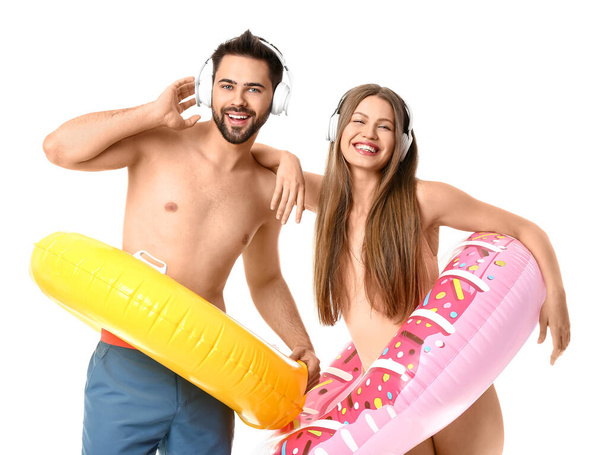 Young couple with headphones and inflatable rings on white background - Zdjęcie, obraz