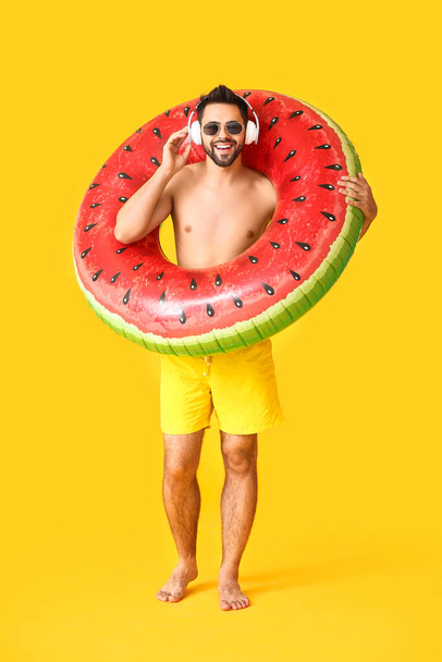 Young man with headphones and inflatable ring on color background - Photo, Image