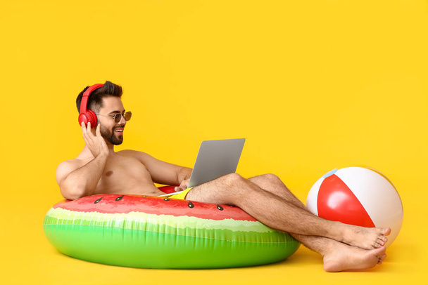 Young man with headphones, inflatable ring and laptop on color background - Фото, зображення