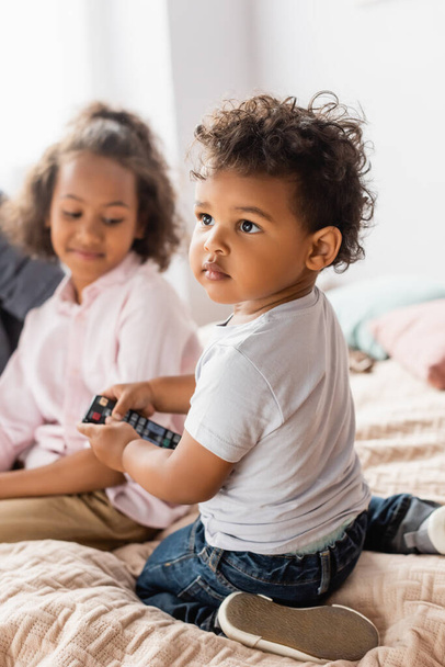 foco seletivo do menino afro-americano em t-shirt branca segurando controlador remoto tv perto da irmã - Foto, Imagem
