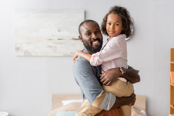 молодой африканский американец отец держит ребенка на руках, глядя в камеру вместе - Фото, изображение